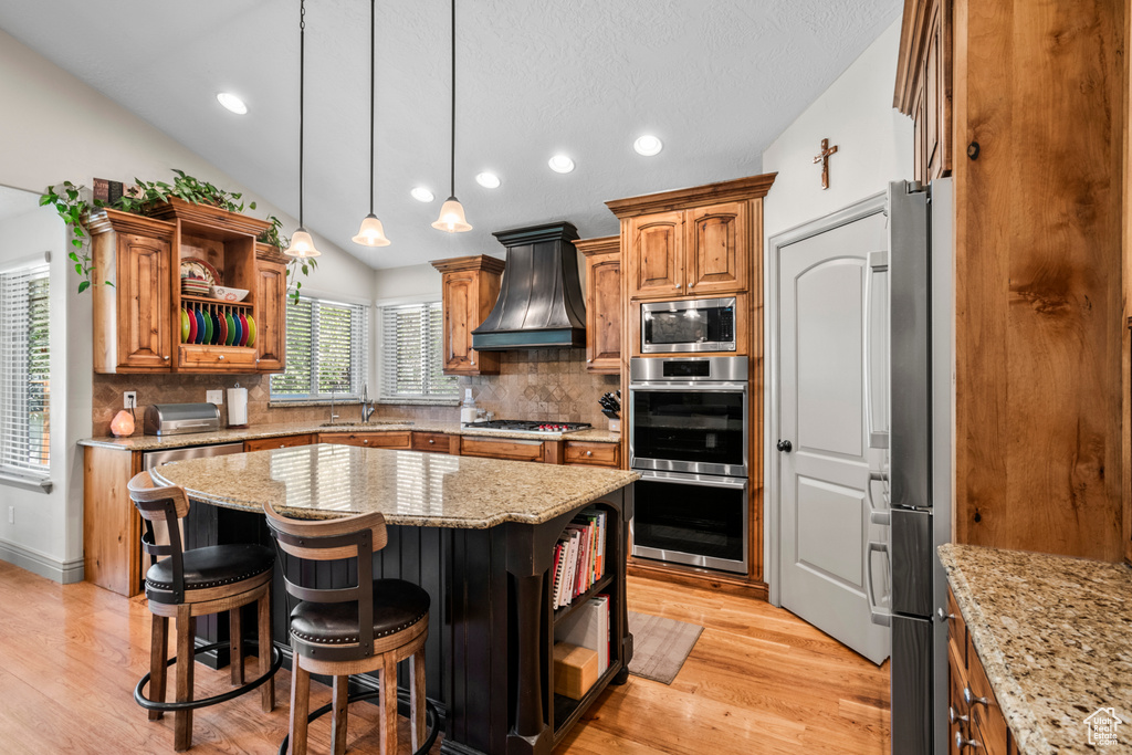 Kitchen featuring a kitchen island, appliances with stainless steel finishes, open shelves, a sink, and premium range hood