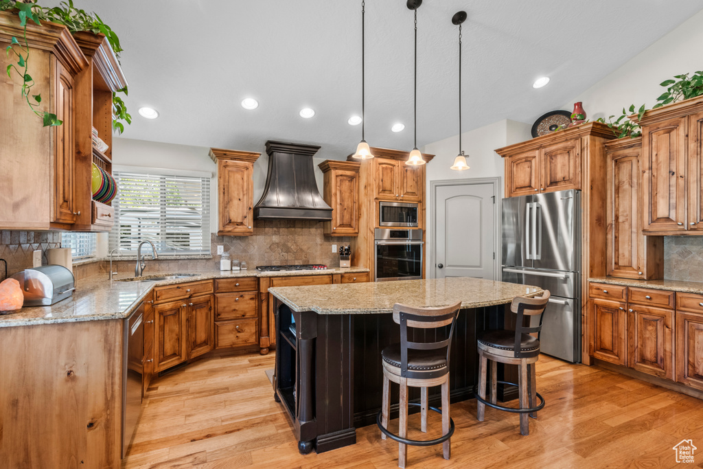 Kitchen featuring a kitchen island, backsplash, a sink, premium range hood, and stainless steel appliances