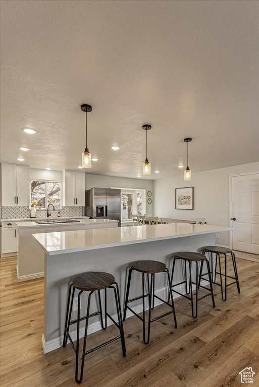 Kitchen with stainless steel fridge, a sink, light wood finished floors, backsplash, and a spacious island