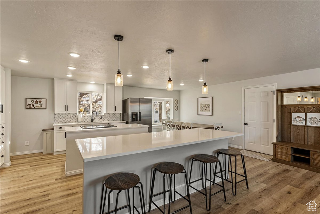 Kitchen featuring a large island, a kitchen breakfast bar, stainless steel fridge, tasteful backsplash, and light wood-style flooring