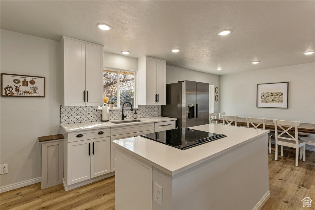 Kitchen featuring a sink, stainless steel fridge with ice dispenser, stovetop with downdraft, and light wood-style flooring