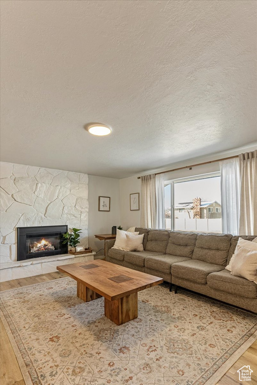 Living area with a textured ceiling, a stone fireplace, and wood finished floors