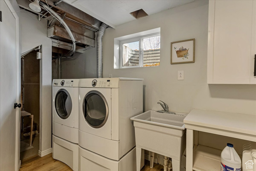 Clothes washing area with light wood-style floors, laundry area, a sink, and washer and clothes dryer