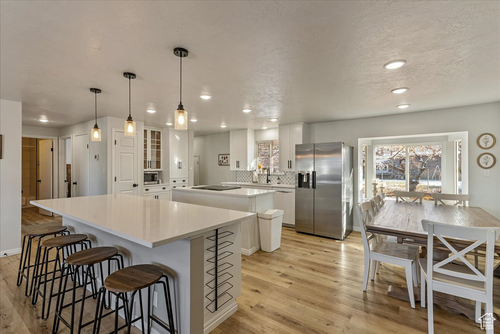 Kitchen featuring white cabinets, light wood-style flooring, stainless steel appliances, a kitchen bar, and a kitchen island