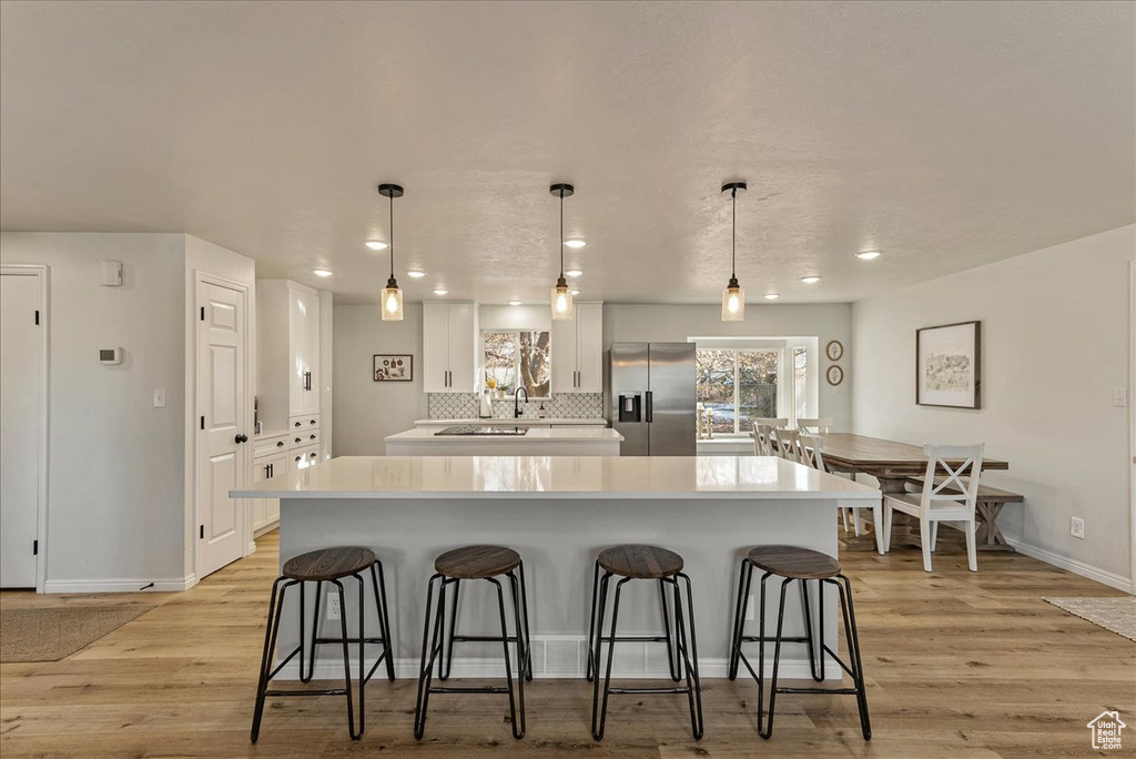 Kitchen with stainless steel fridge with ice dispenser, light countertops, a breakfast bar area, white cabinetry, and baseboards