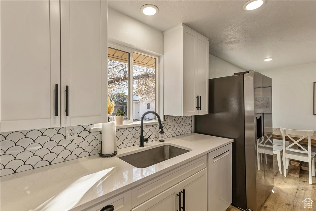 Kitchen with appliances with stainless steel finishes, a sink, light countertops, white cabinetry, and backsplash