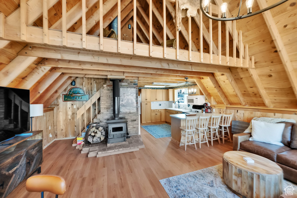 Living room with a wood stove, wooden walls, light wood-type flooring, a chandelier, and lofted ceiling with beams
