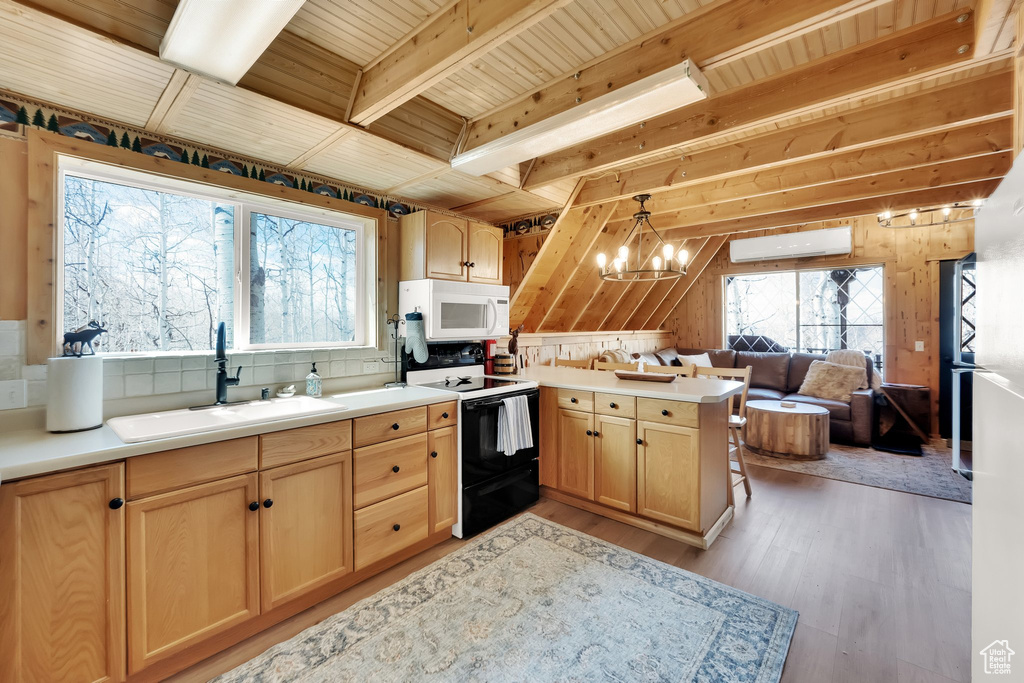Kitchen featuring a sink, a peninsula, light brown cabinets, white microwave, and electric stove