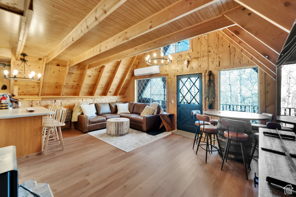 Living room with lofted ceiling with beams, an AC wall unit, a chandelier, wooden walls, and light wood-style flooring