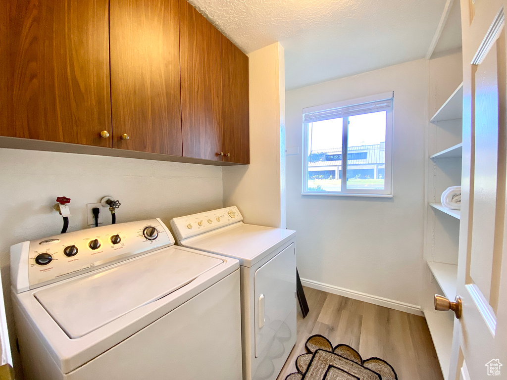 Clothes washing area featuring cabinet space, light wood finished floors, a textured ceiling, baseboards, and washer and clothes dryer