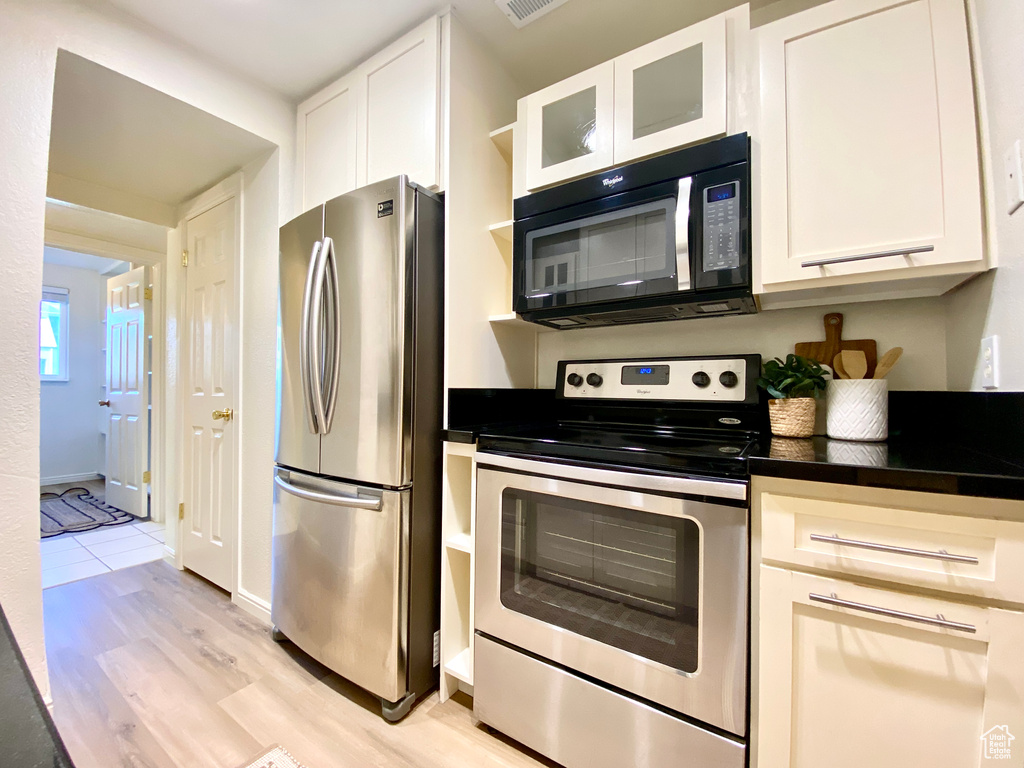 Kitchen featuring dark countertops, appliances with stainless steel finishes, light wood-style flooring, and white cabinetry