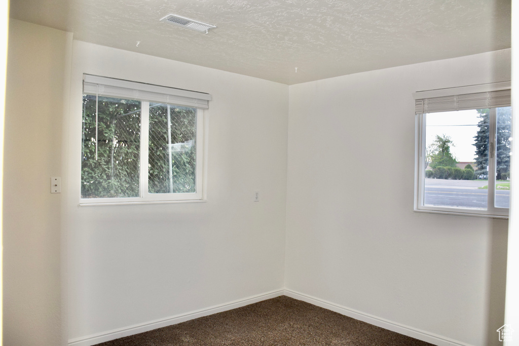 Unfurnished room with plenty of natural light, dark colored carpet, a textured ceiling, and visible vents
