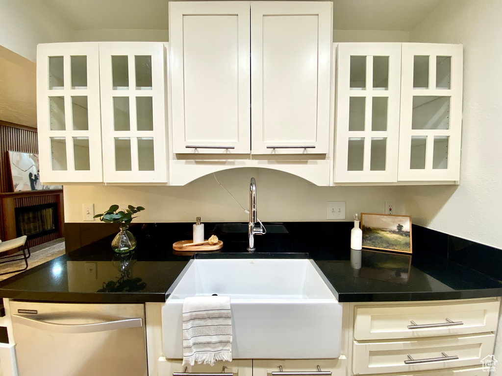 Kitchen featuring a sink, dark countertops, stainless steel dishwasher, and white cabinetry