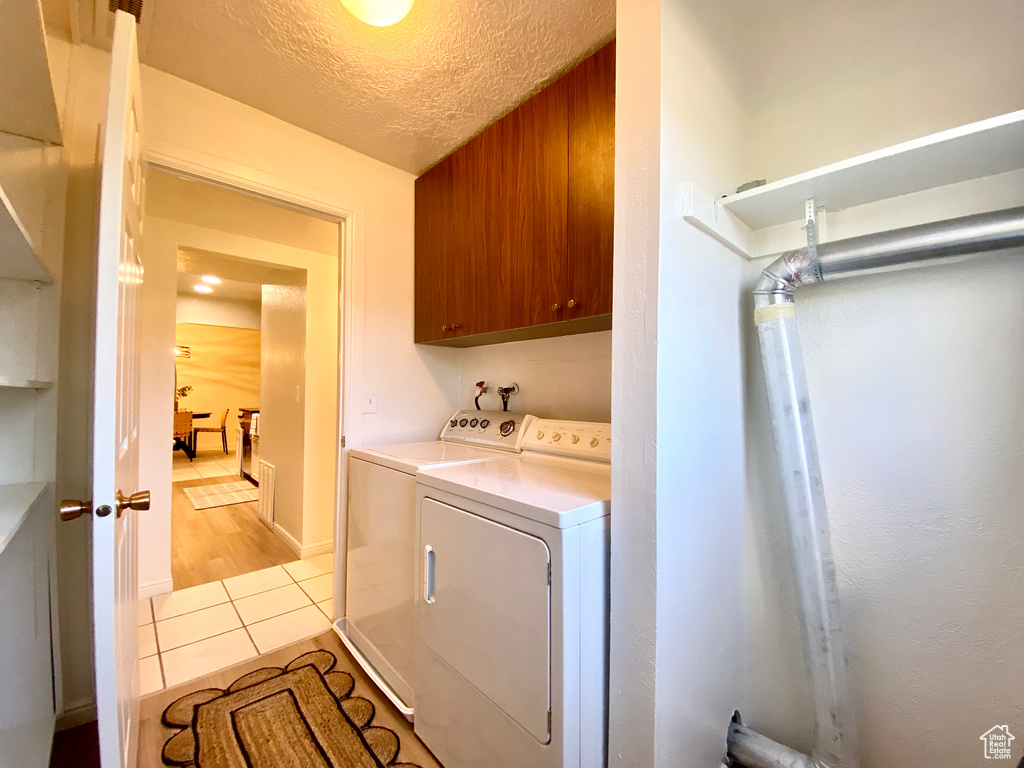 Clothes washing area featuring a textured ceiling, cabinet space, light tile patterned floors, and washer and dryer