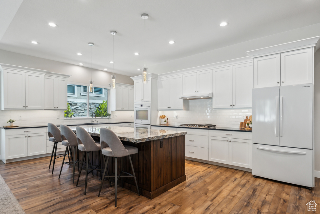 Kitchen with dark wood-type flooring, a center island, decorative backsplash, and white appliances