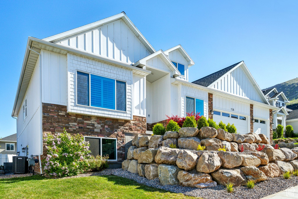 Modern inspired farmhouse with a front lawn, stone siding, a garage, board and batten siding, and central AC unit