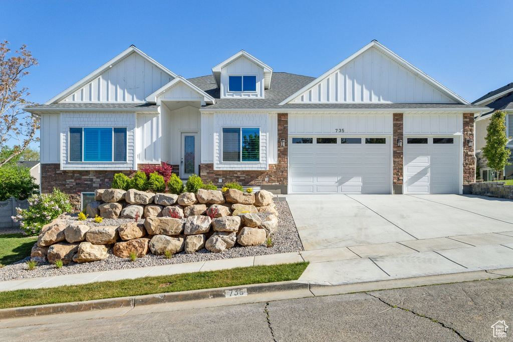 View of front of home with roof with shingles, an attached garage, stone siding, board and batten siding, and concrete driveway