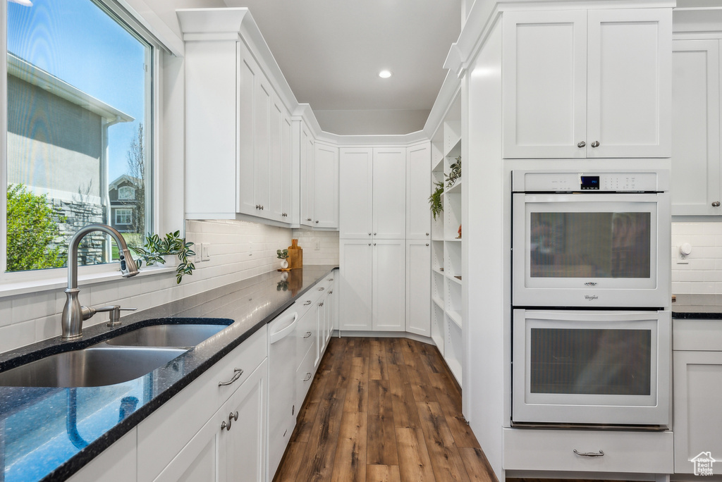 Kitchen with white appliances, white cabinets, dark stone counters, dark wood finished floors, and a sink
