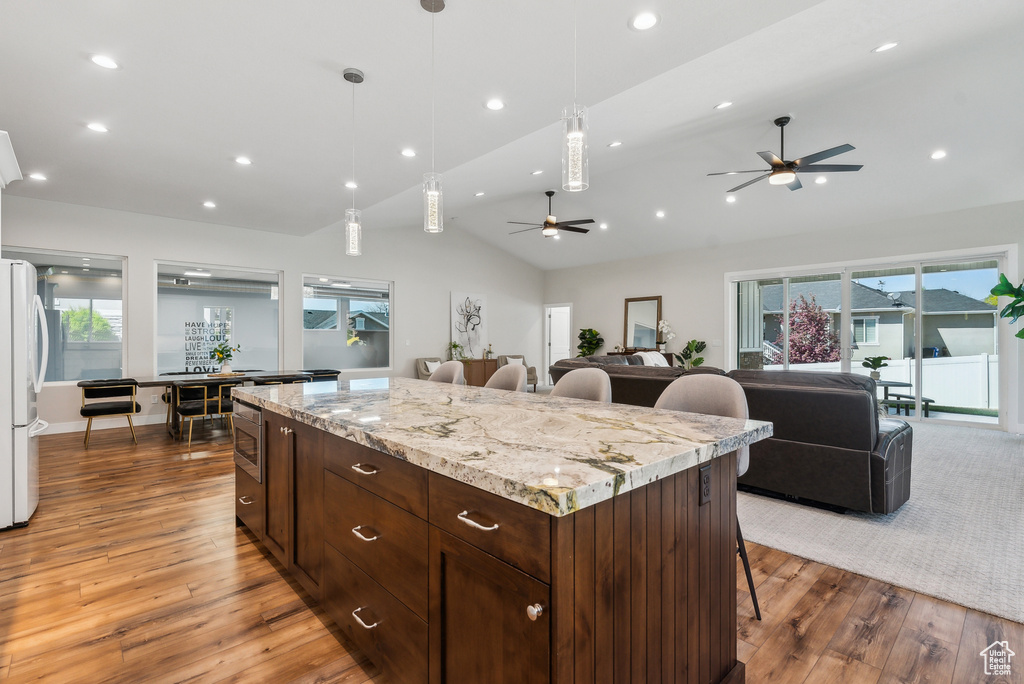 Kitchen featuring a kitchen bar, a ceiling fan, wood finished floors, stainless steel microwave, and open floor plan