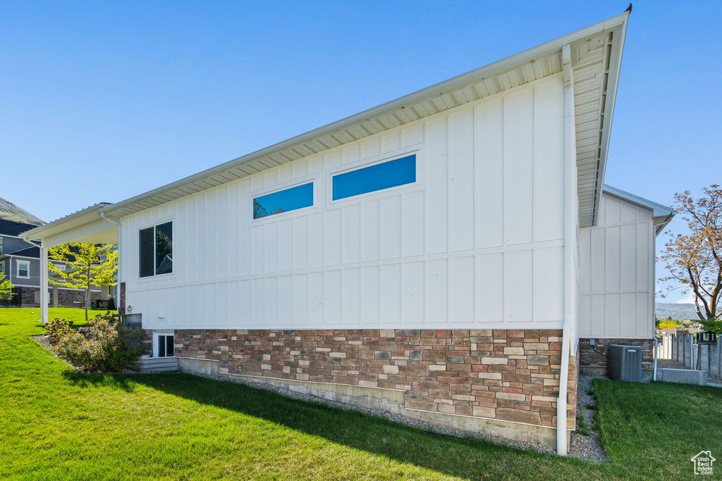 View of side of property with board and batten siding, central air condition unit, and a yard