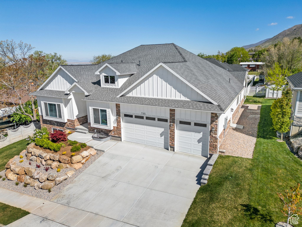 View of front of property featuring board and batten siding, driveway, roof with shingles, a garage, and stone siding