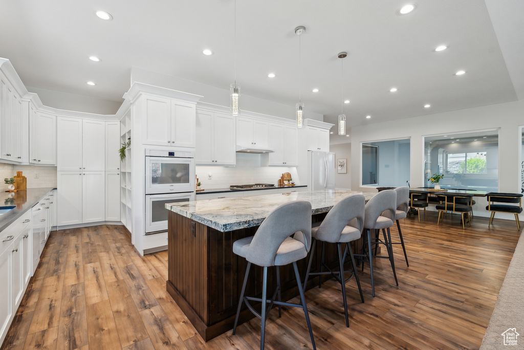 Kitchen with dark wood-style flooring, decorative backsplash, white appliances, and a spacious island