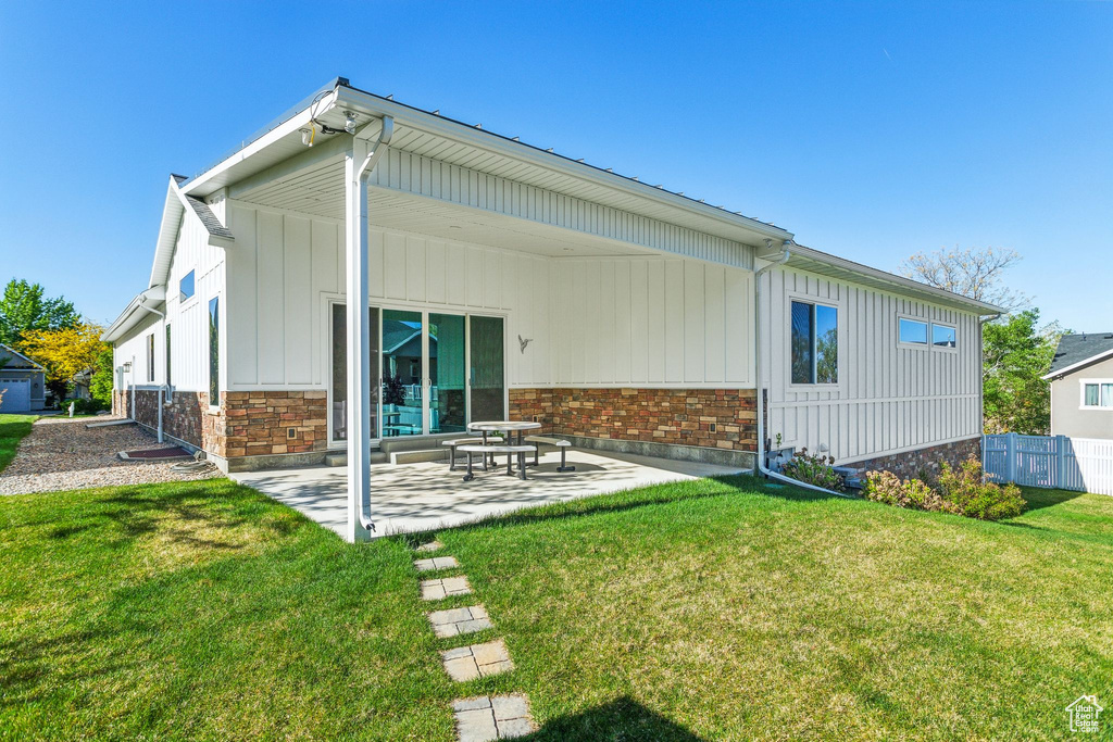 Rear view of property featuring a patio, board and batten siding, a lawn, and fence