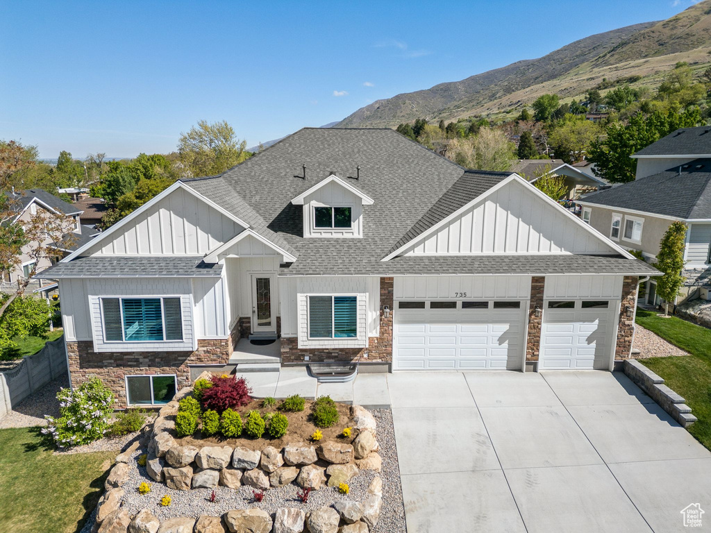 View of front facade featuring stone siding, roof with shingles, board and batten siding, concrete driveway, and an attached garage