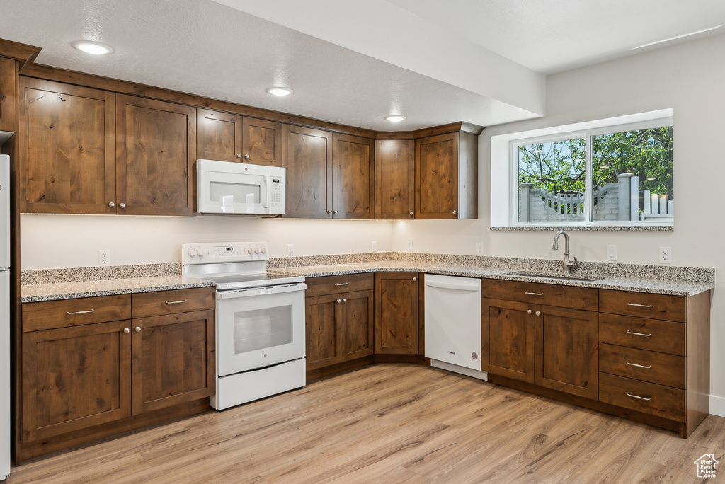 Kitchen featuring a sink, light wood finished floors, white appliances, and light stone counters