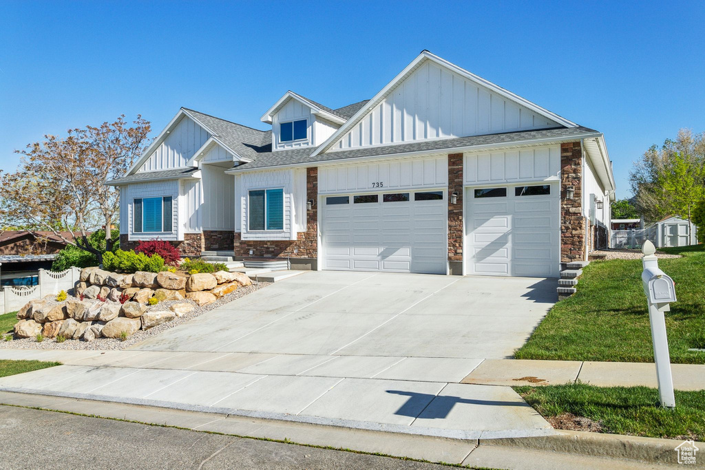 View of front of property with stone siding, roof with shingles, board and batten siding, an attached garage, and driveway
