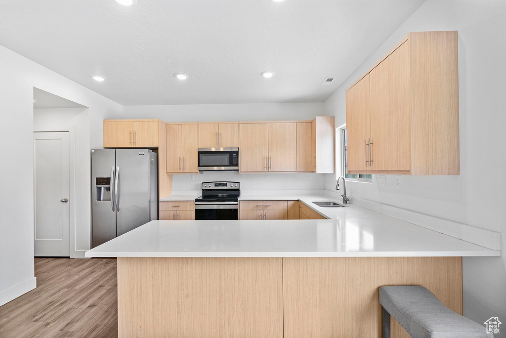 Kitchen featuring a sink, a peninsula, light wood-style floors, light brown cabinets, and stainless steel appliances