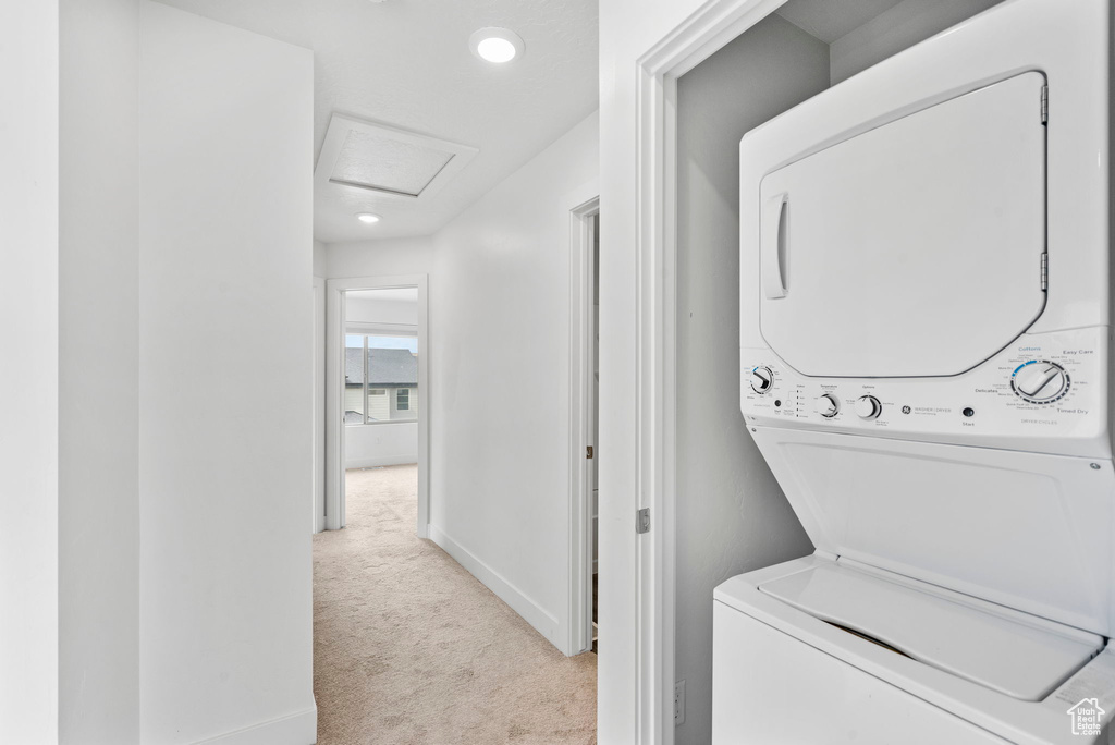 Laundry room with carpet floors, laundry area, baseboards, attic access, and stacked washer / drying machine