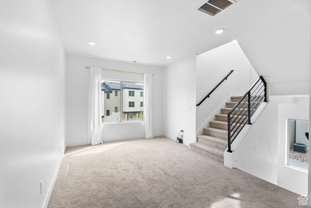 Unfurnished living room featuring recessed lighting, stairway, visible vents, and carpet