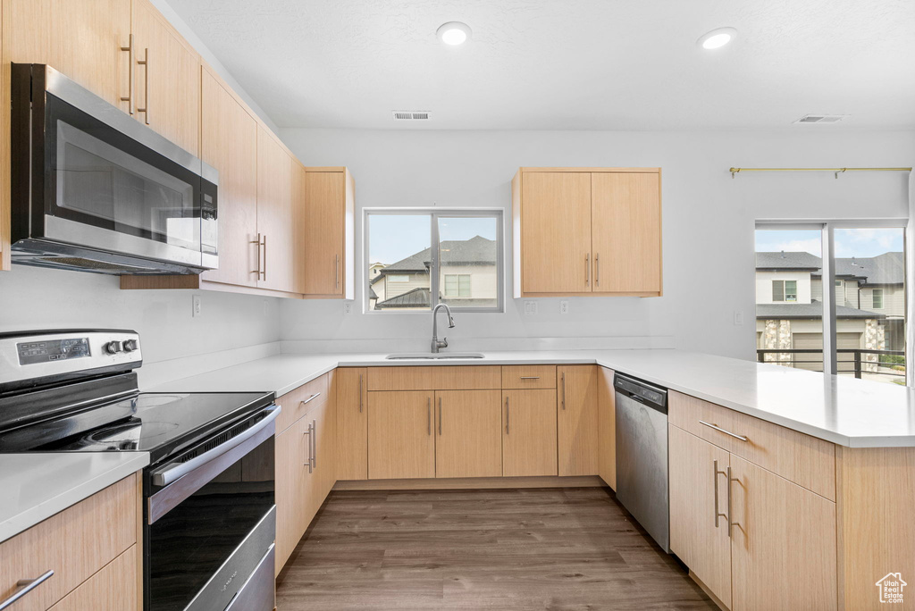 Kitchen featuring light brown cabinetry, appliances with stainless steel finishes, a peninsula, and a sink