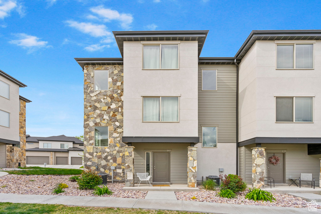 Modern home with central air condition unit, stucco siding, and stone siding