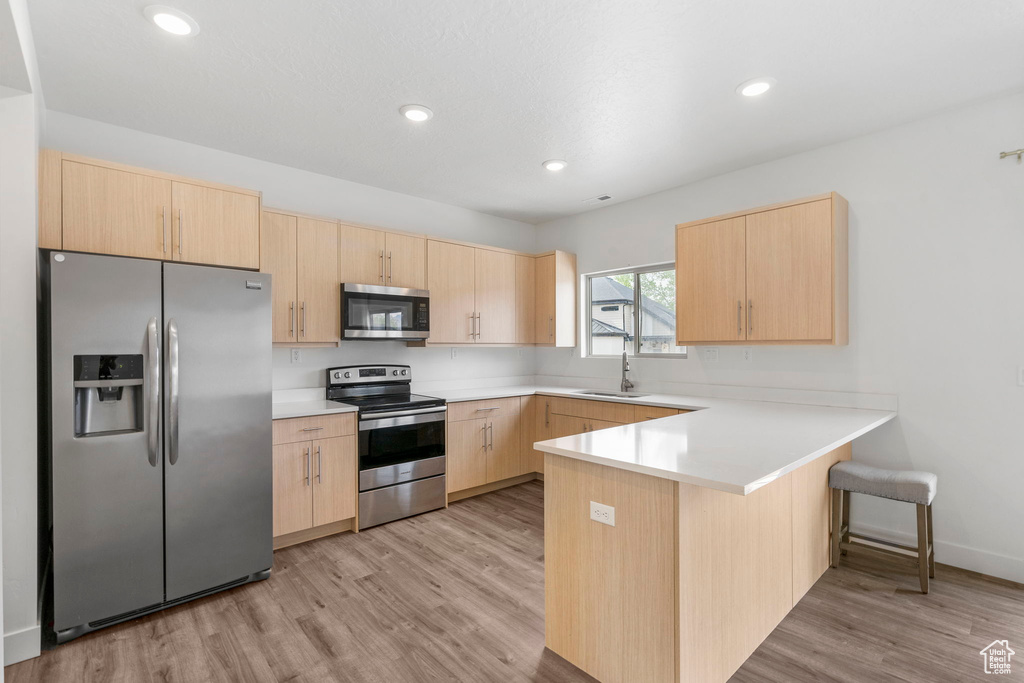 Kitchen with light brown cabinetry, light wood-type flooring, a sink, a peninsula, and stainless steel appliances