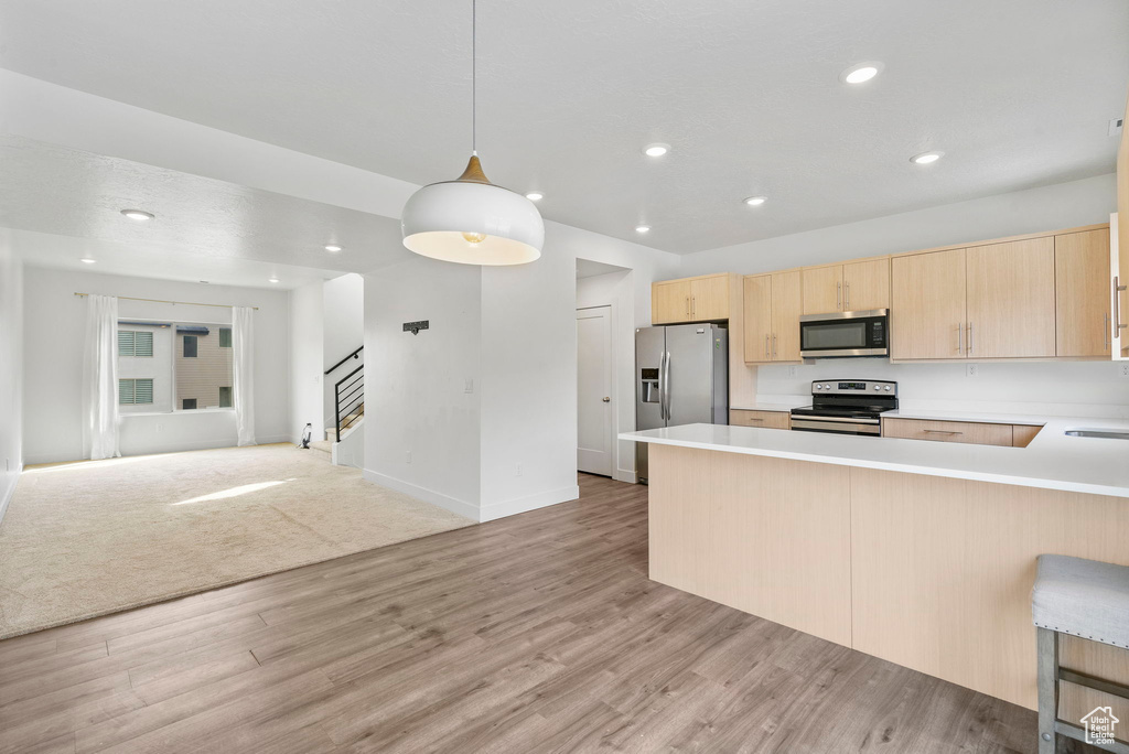 Kitchen featuring light countertops, a peninsula, open floor plan, light brown cabinets, and stainless steel appliances