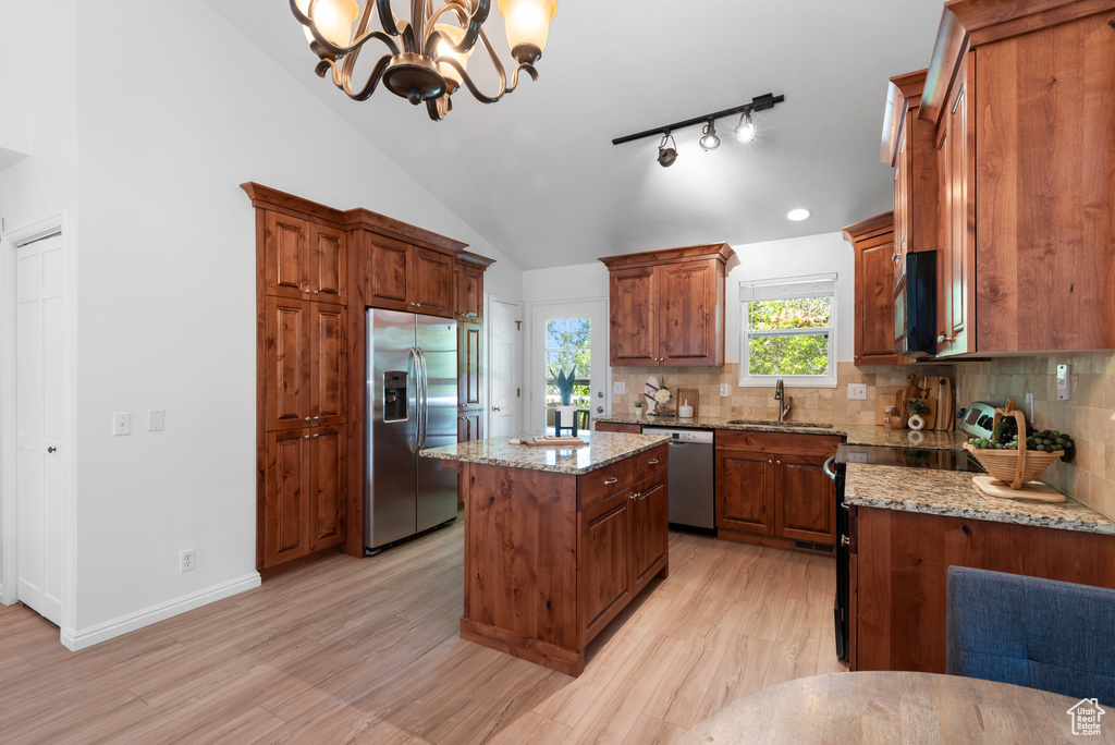 Kitchen with light stone countertops, appliances with stainless steel finishes, a sink, light wood-style flooring, and tasteful backsplash