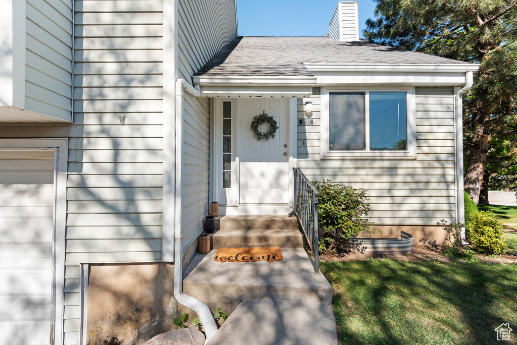 Entrance to property with a lawn and roof with shingles