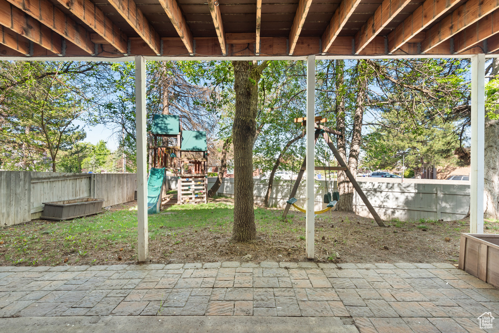 View of patio with a playground and a fenced backyard