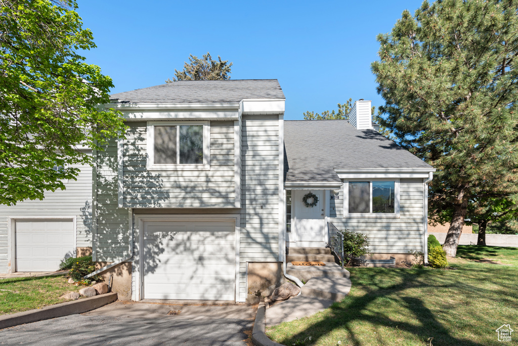 View of front of home with a chimney, an attached garage, a front lawn, and aphalt driveway