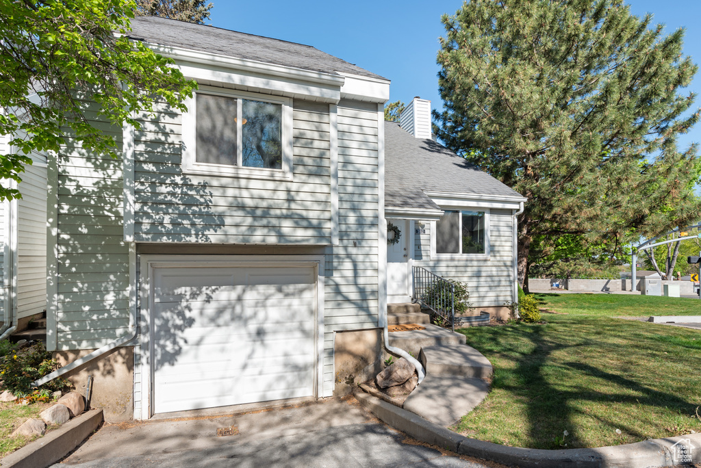 View of front of property with an attached garage, a front lawn, entry steps, a chimney, and driveway