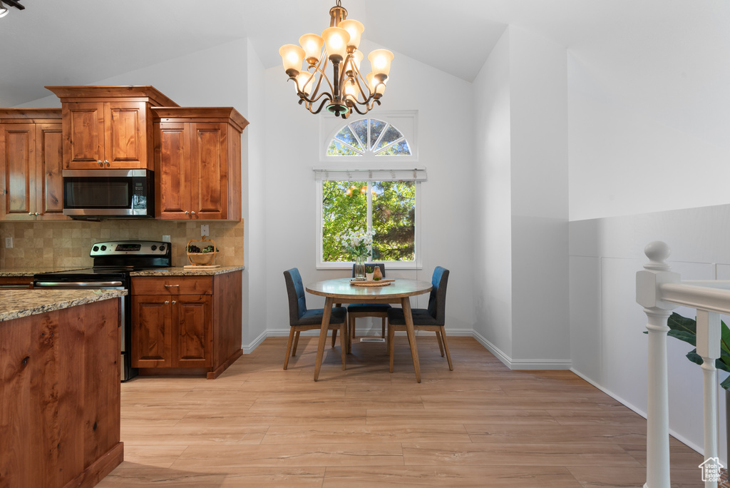 Kitchen featuring backsplash, stainless steel appliances, brown cabinetry, and lofted ceiling