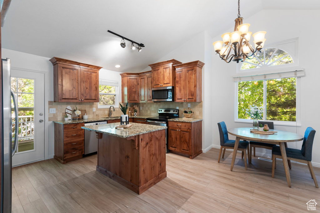 Kitchen featuring stainless steel appliances, vaulted ceiling, decorative backsplash, and a chandelier