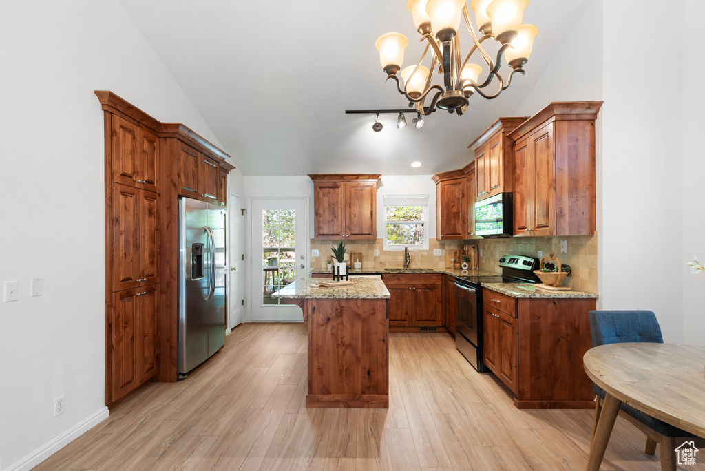 Kitchen with decorative backsplash, a kitchen island, light wood-style flooring, appliances with stainless steel finishes, and a notable chandelier
