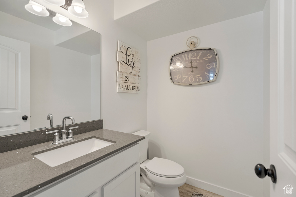Half bathroom featuring toilet, wood finished floors, and vanity