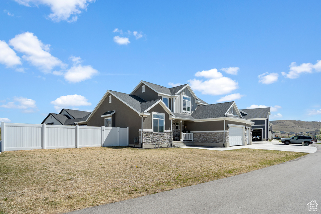 Craftsman-style house with fence, an attached garage, stone siding, a front yard, and concrete driveway