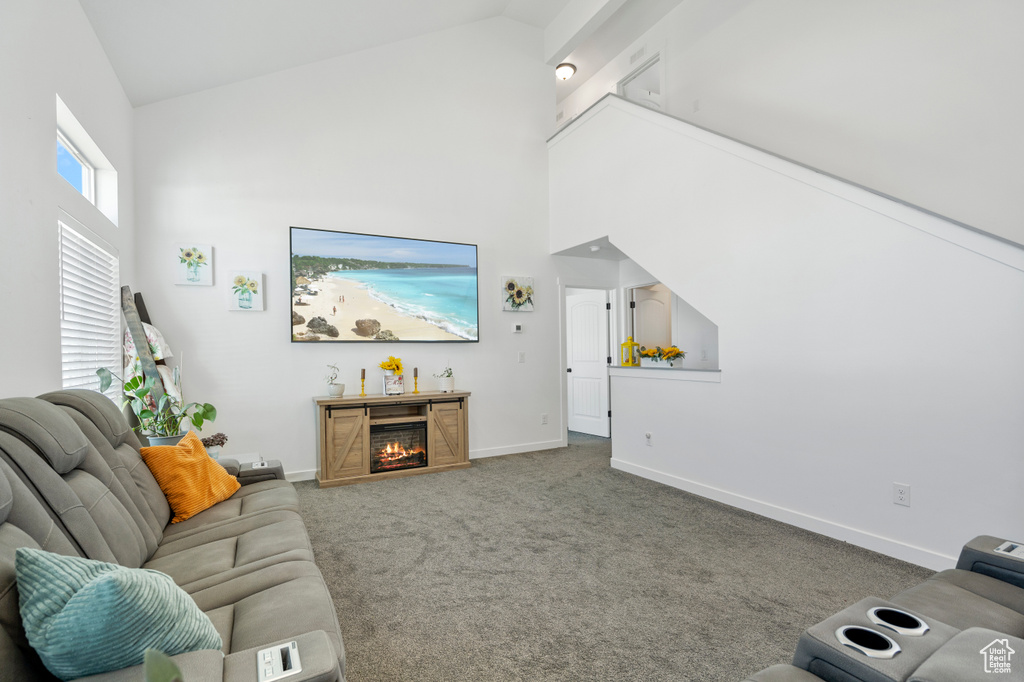 Carpeted living area with baseboards, a lit fireplace, and high vaulted ceiling
