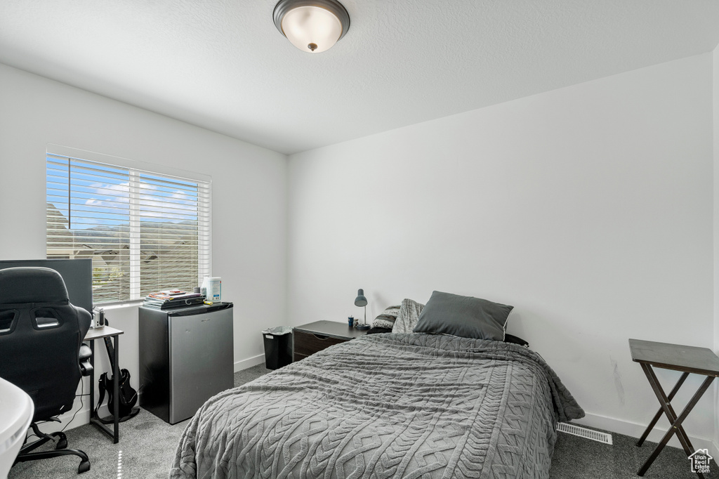 Carpeted bedroom with baseboards, freestanding refrigerator, and visible vents