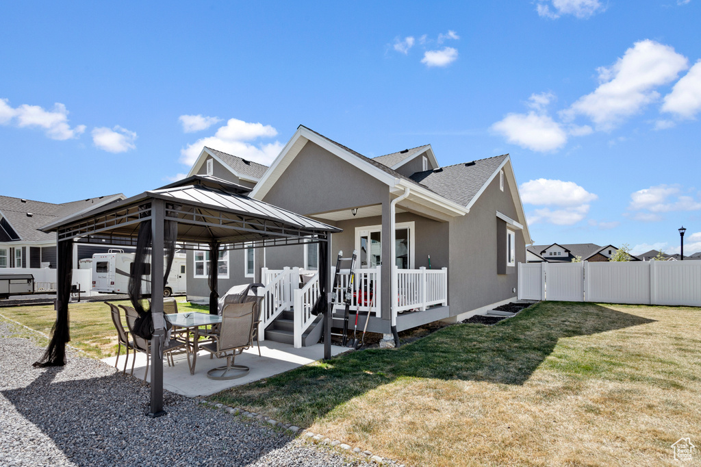 Rear view of property featuring fence, a wooden deck, a patio area, a gazebo, and a yard